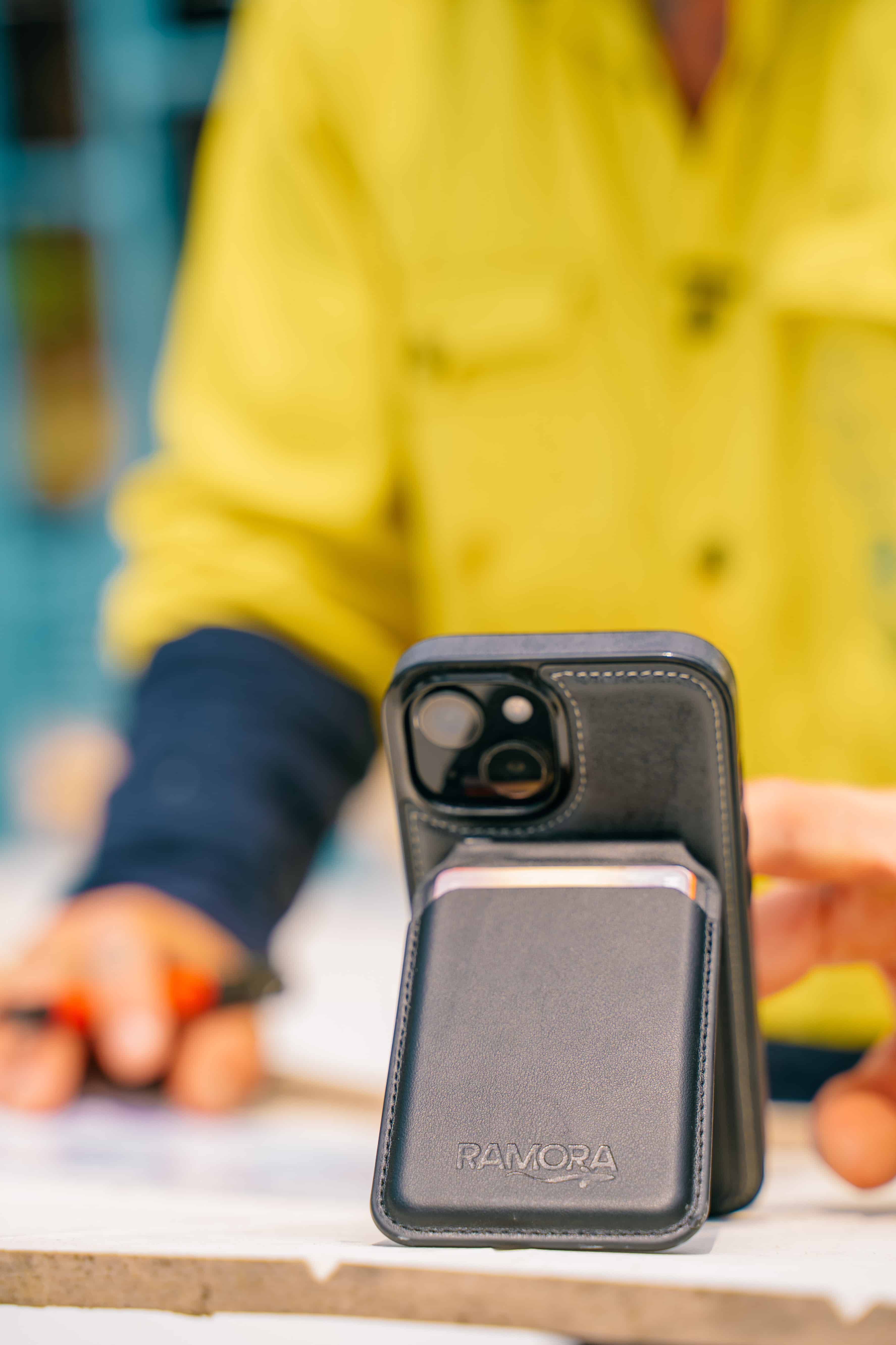 Person holding a phone with a black Ramora case, blurred background